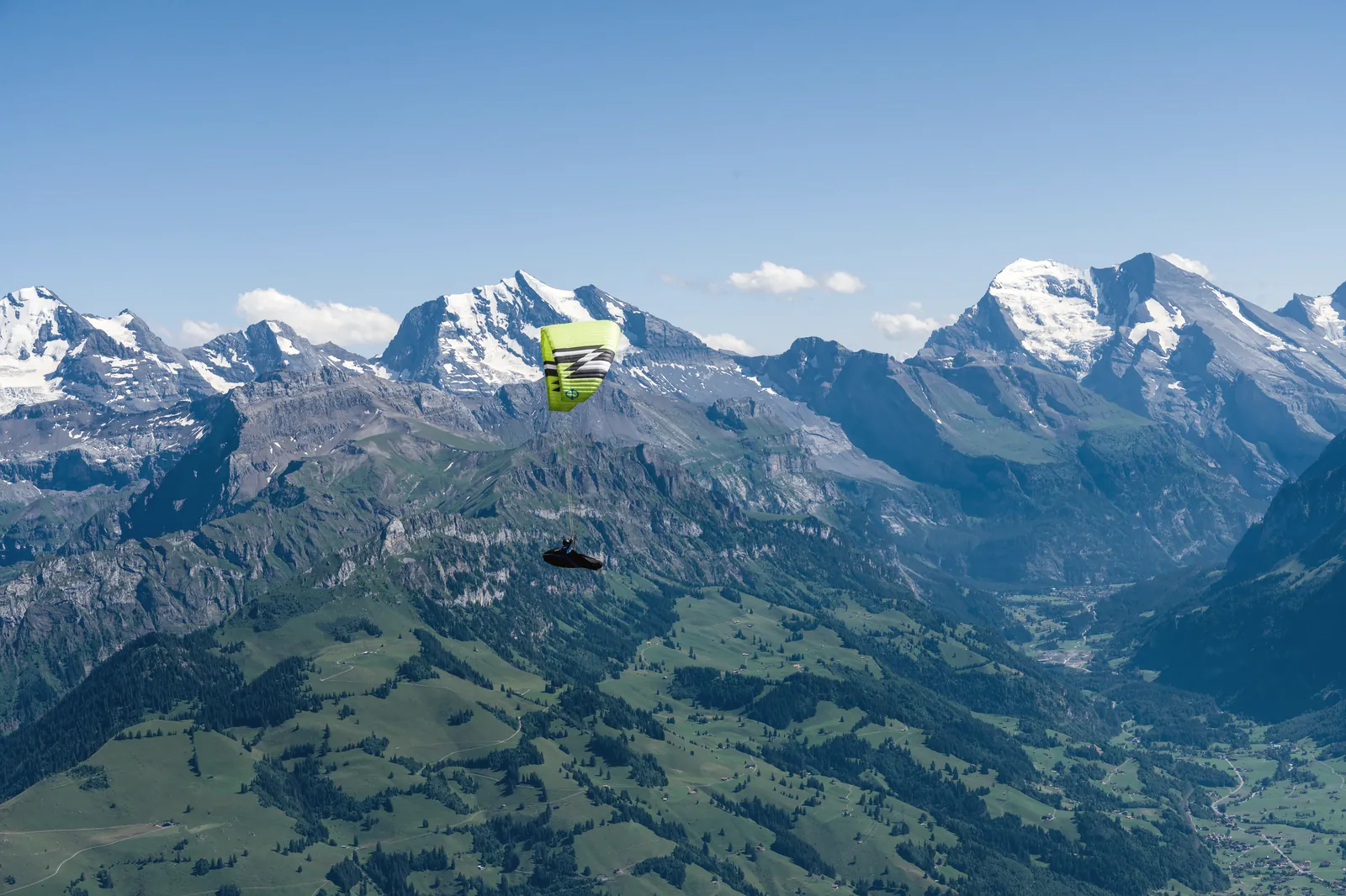 A paraglider soars above the majestic peaks of the Swiss Alps under a clear blue sky.