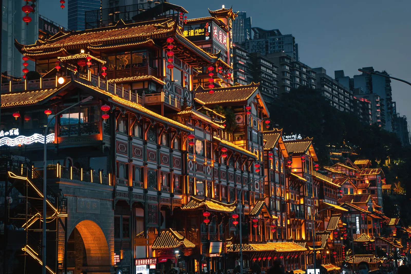 Night view of illuminated traditional Chinese architecture in Chongqing's urban setting.
