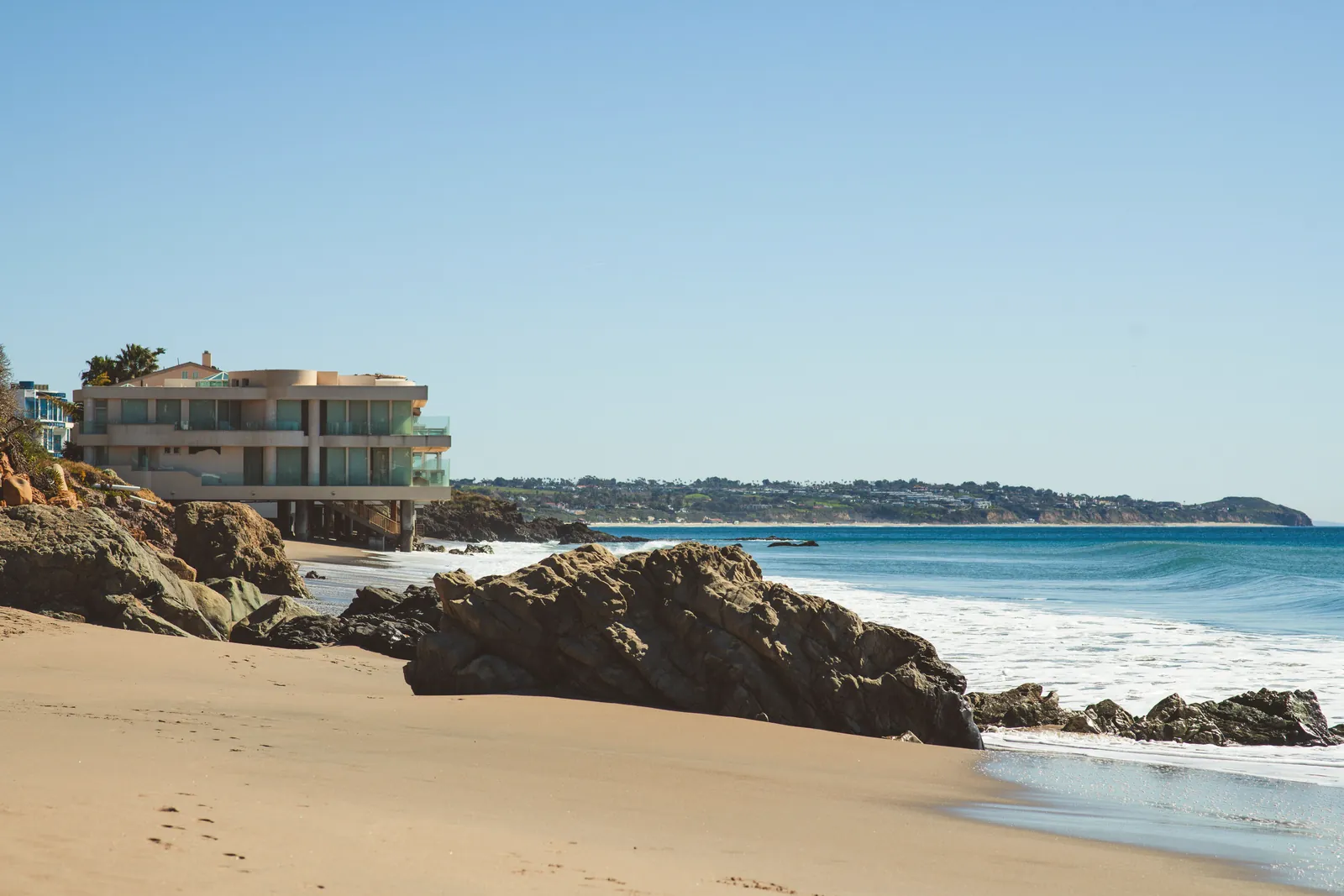 Stylish beach house overlooking the ocean, surrounded by rocks and sandy shores.