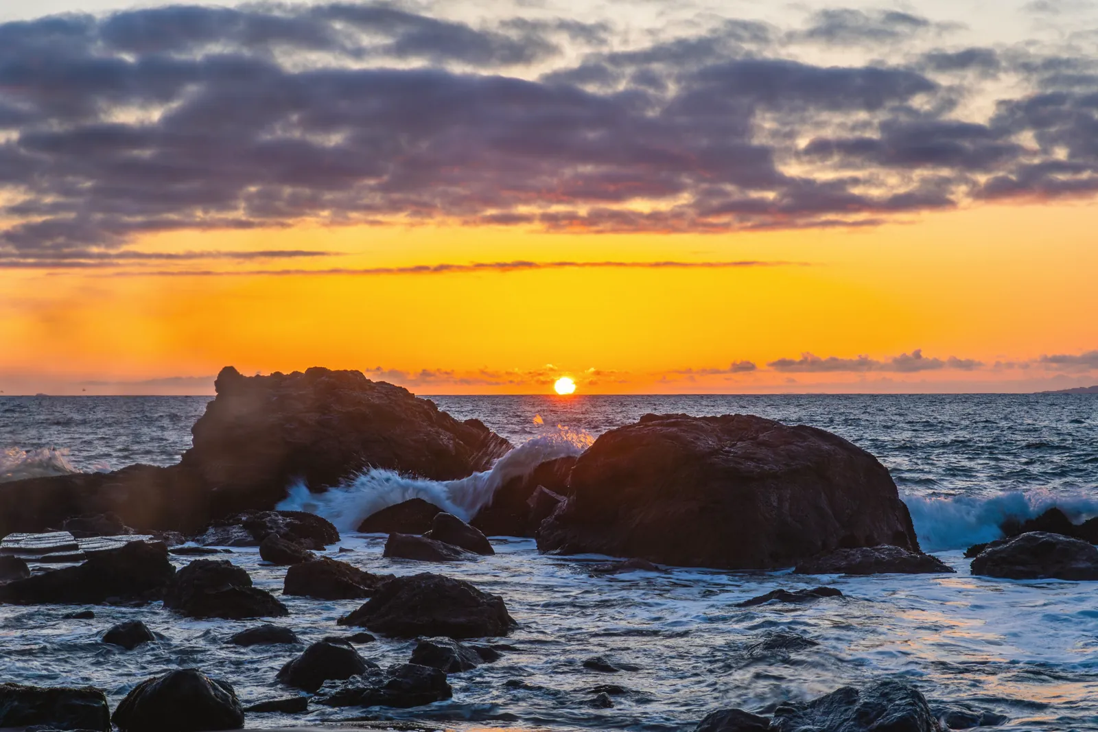 Breathtaking sunset over a rocky coastline, capturing vibrant colors and dynamic waves.