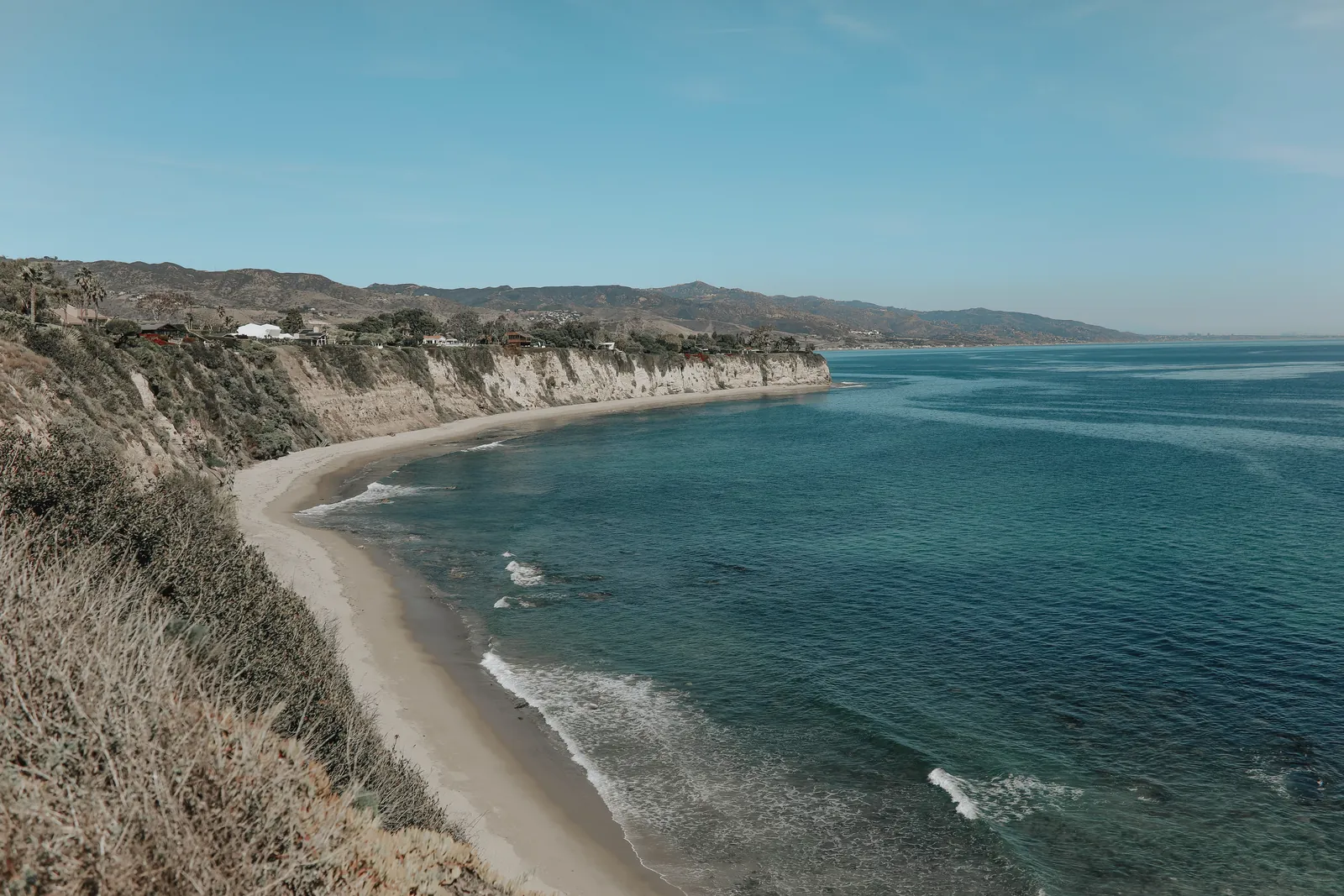 Beautiful panoramic view of rugged cliffs and serene sea under a clear blue sky.
