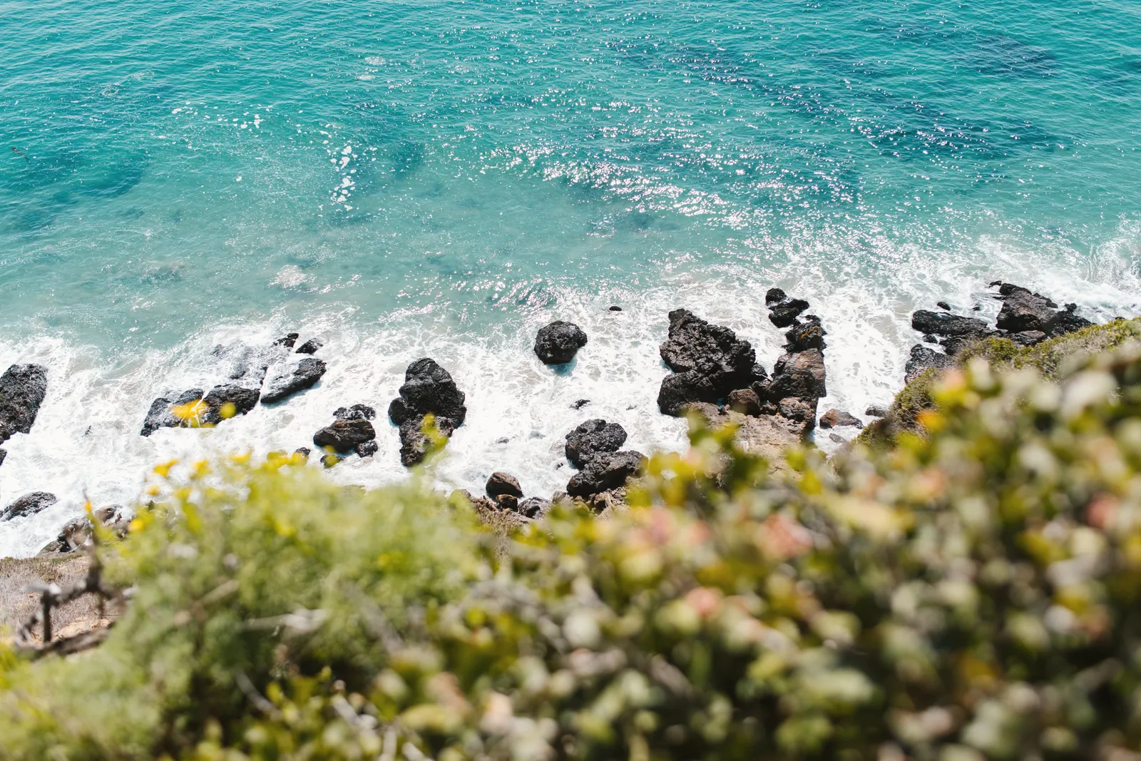 High-angle view of a rocky coastline with vibrant blue ocean waves gently crashing against the shore.