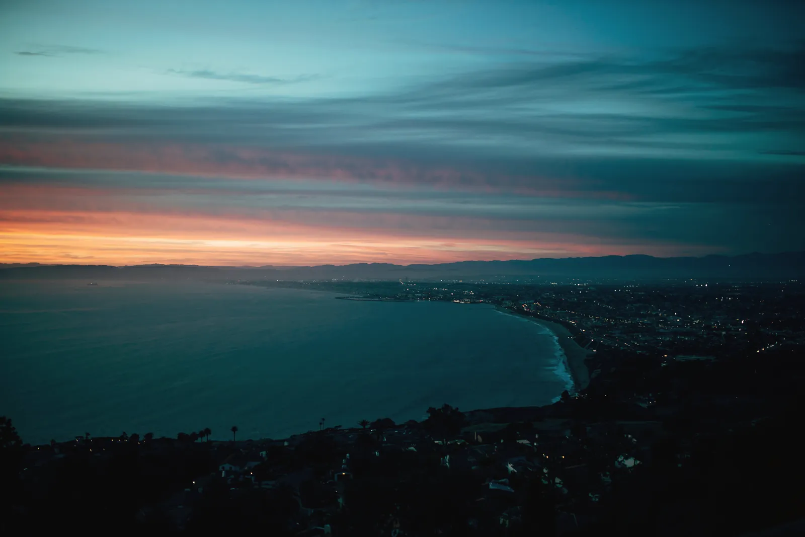 Breathtaking view of a coastal city as twilight descends, blending vibrant skies with city lights.