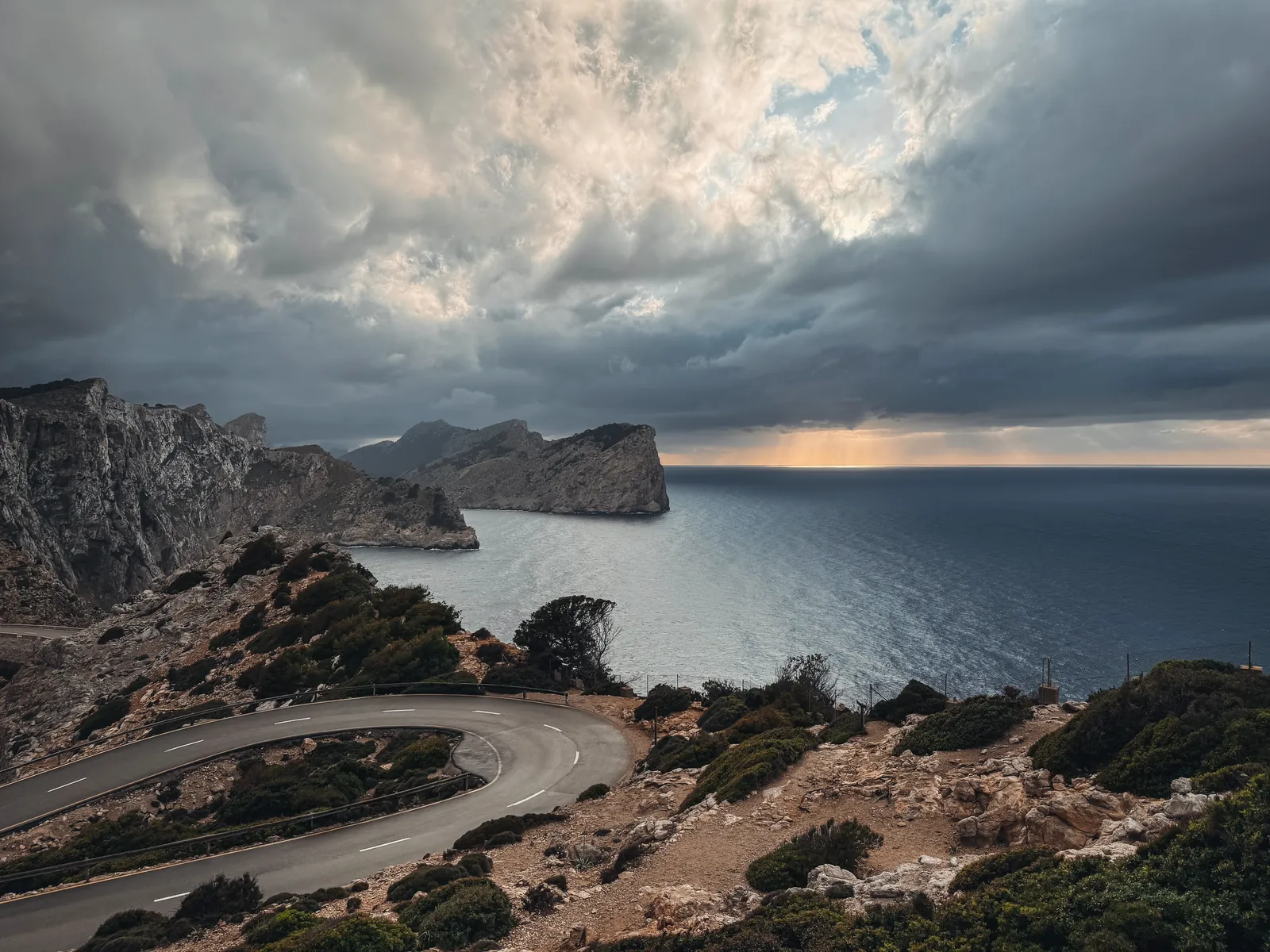 Captivating coastal road view in Mallorca, Spain with dramatic cliffs and sea under a cloudy sky.