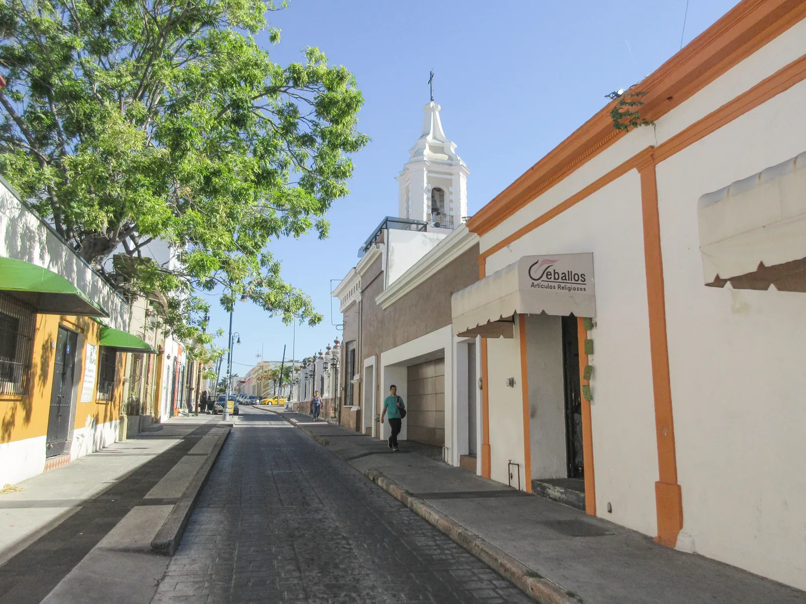 A scenic street view in Manzanillo, Colima featuring traditional architecture and a prominent bell tower.