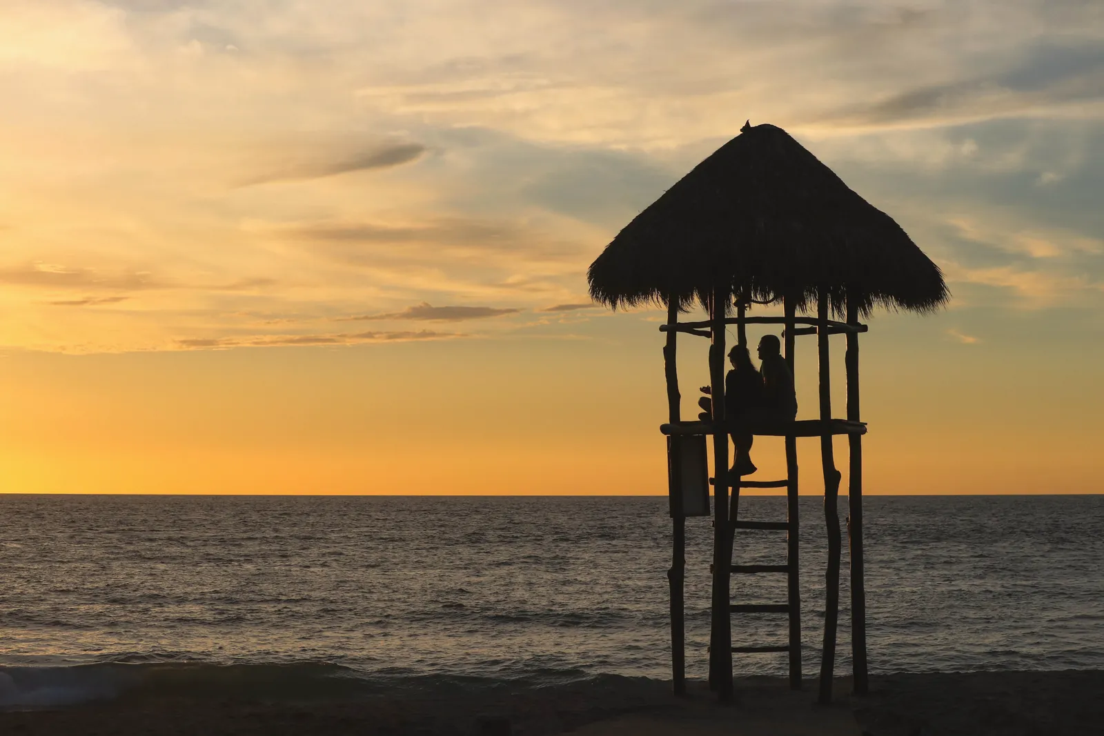 A serene beach scene with a silhouette of a lifeguard tower against a vibrant sunset.