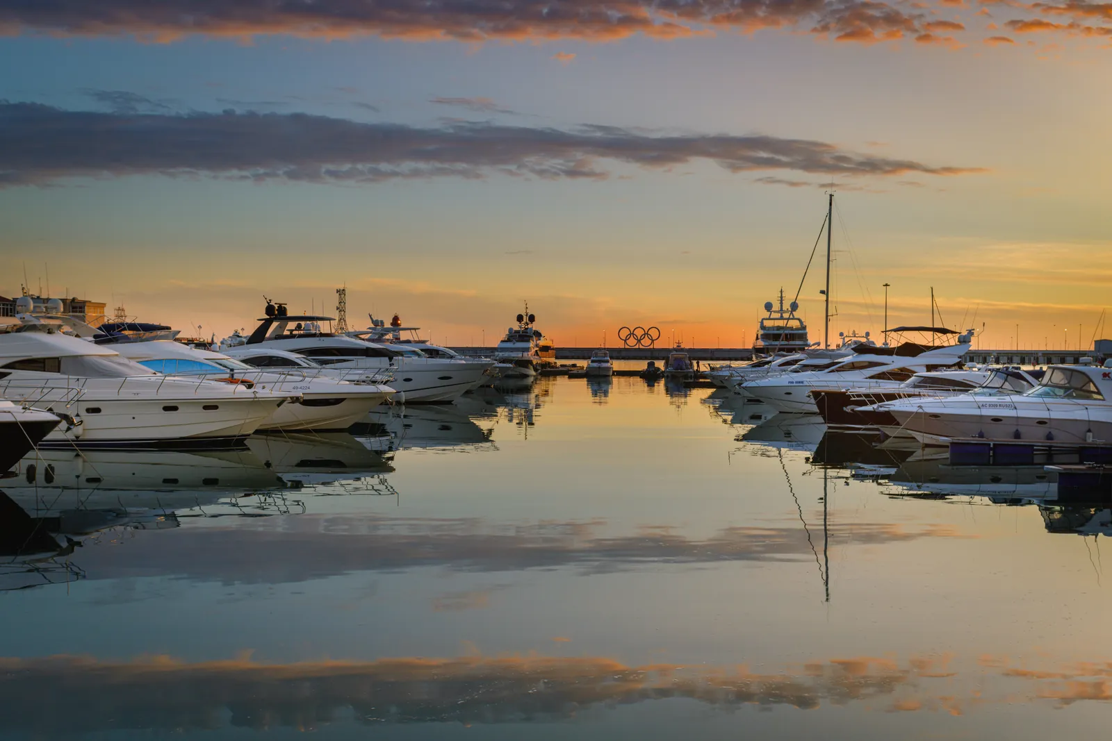 Peaceful harbor scene with yachts docked at sunset under a colorful sky.