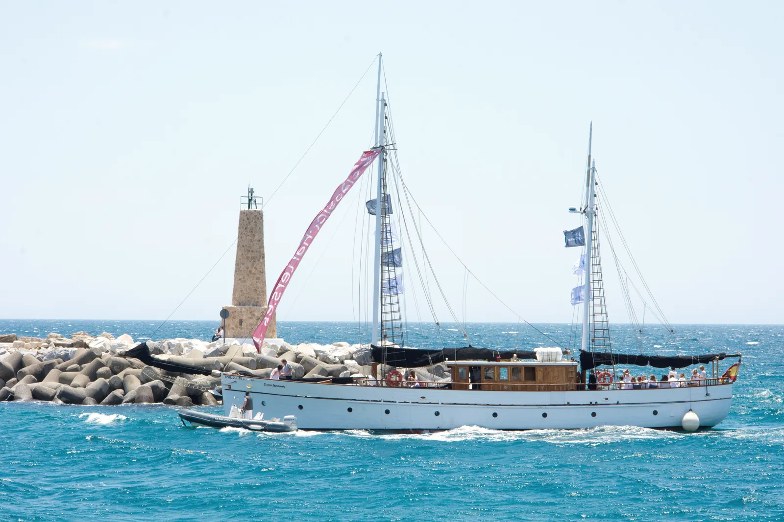 A beautiful yacht sailing near a lighthouse under a clear sky in Marbella, Spain.