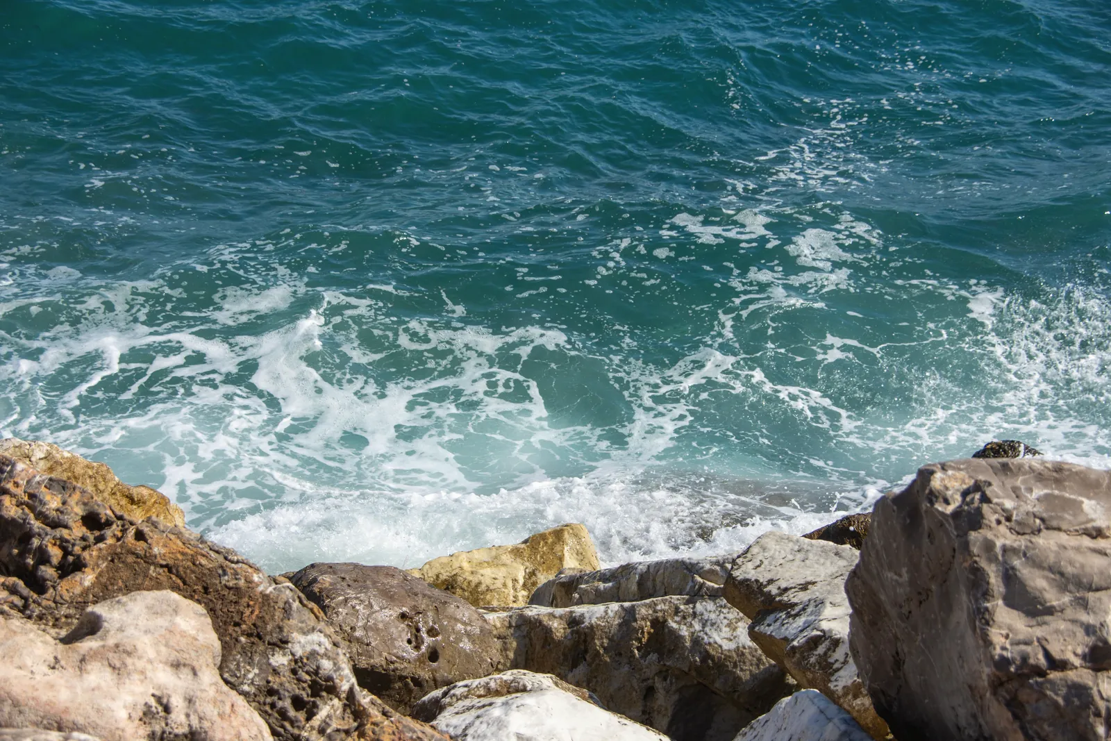 Vivid blue waves crashing against rocky shore in Marbella, Spain, showcasing Mediterranean beauty.