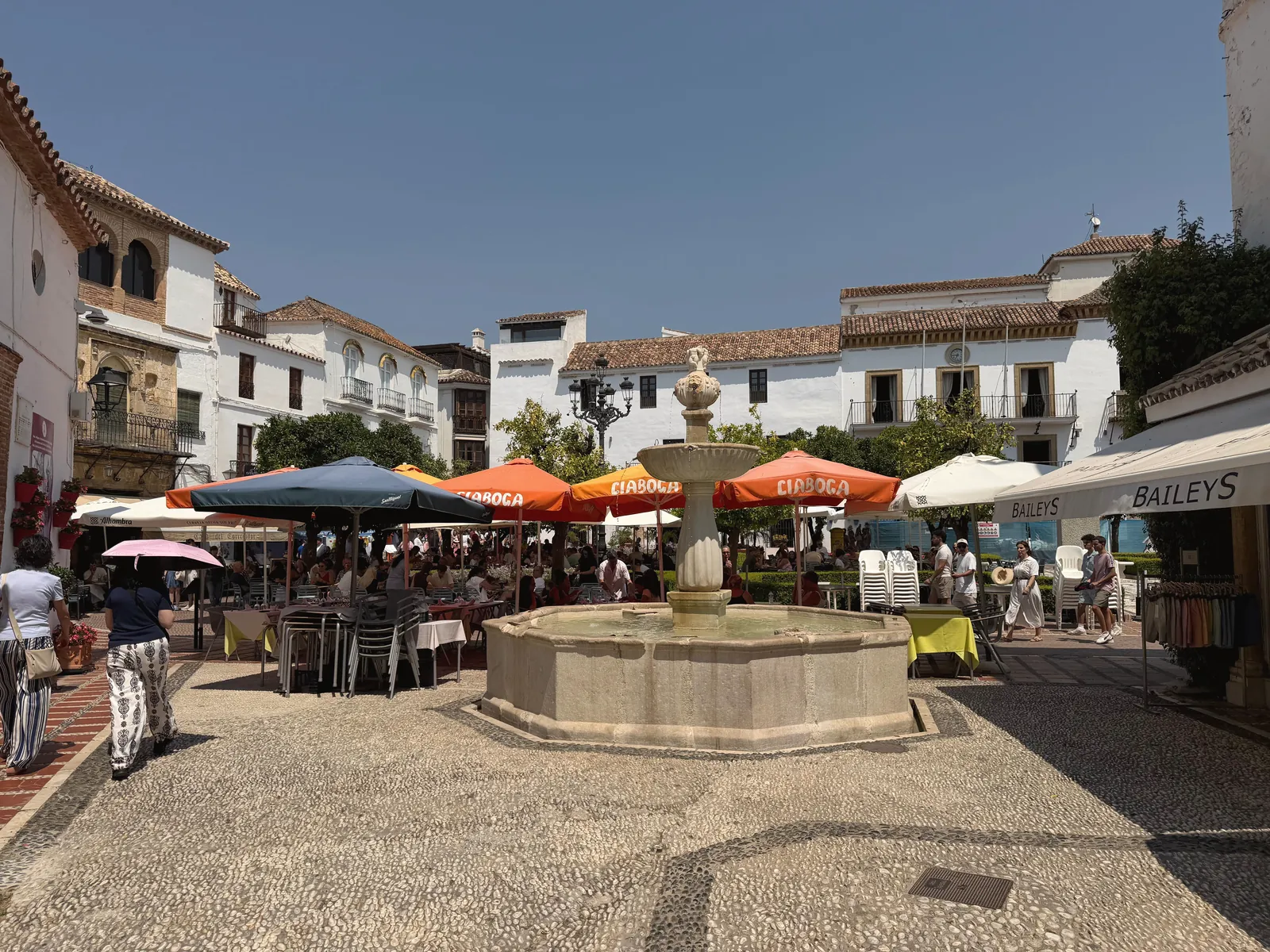 Sunny day in Marbella's picturesque plaza featuring a central fountain and outdoor cafes.