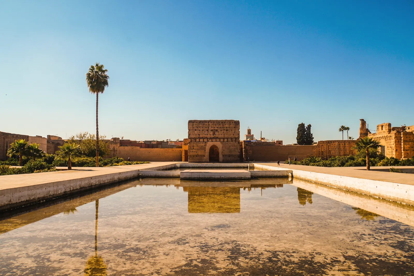 El Badi Palace in Marrakech under a clear blue sky with a reflecting pool in the foreground.