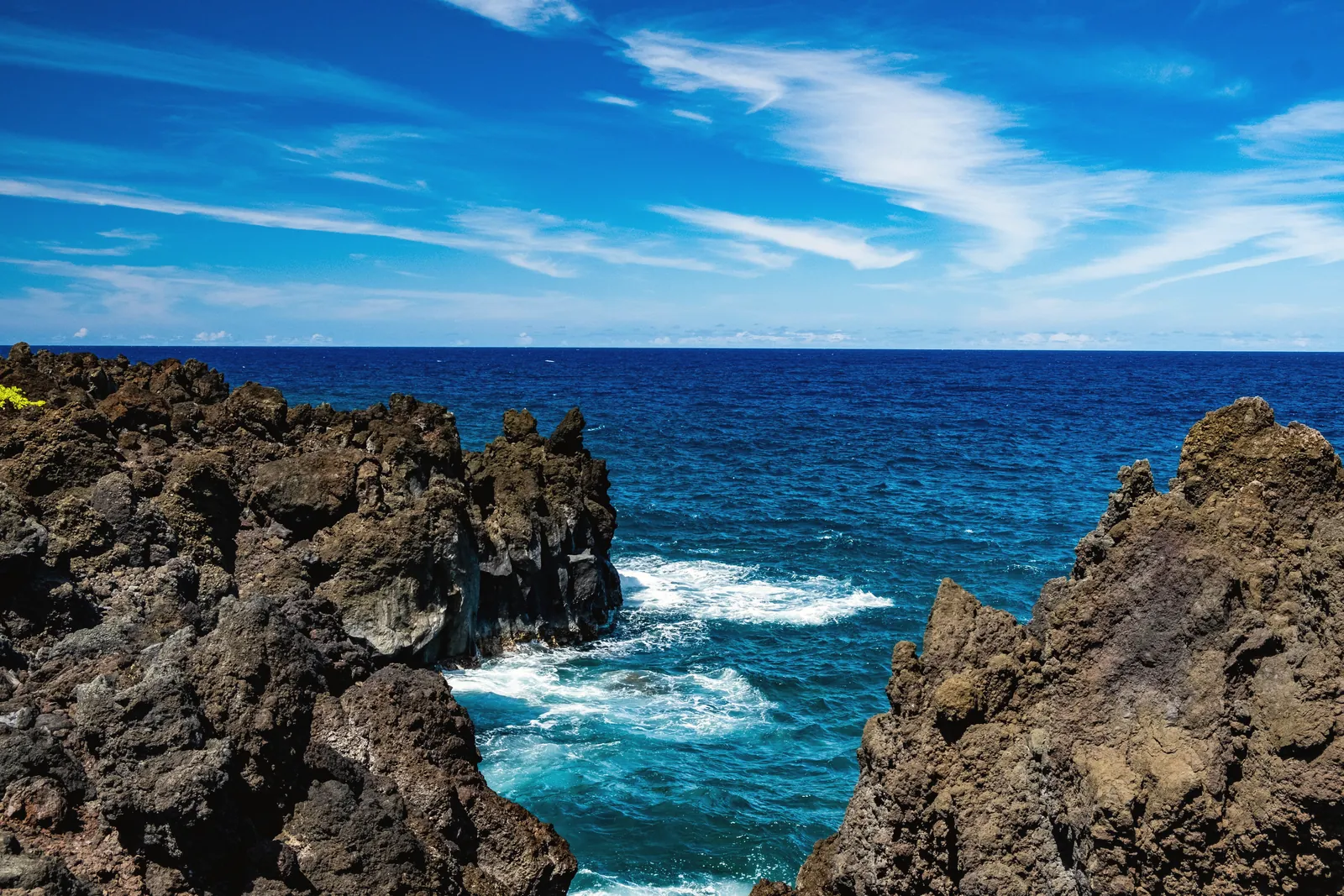 Breathtaking view of rugged rocks and vibrant blue ocean at Hana, Hawaii under a clear sky.