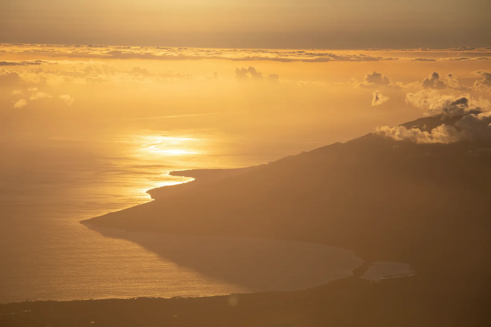 Breathtaking aerial vista of a sunlit coastline at sunset with dramatic clouds.