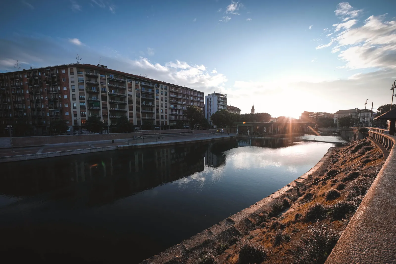 Calm river flowing along embankment in city and reflecting buildings and cloudy blue sky in water