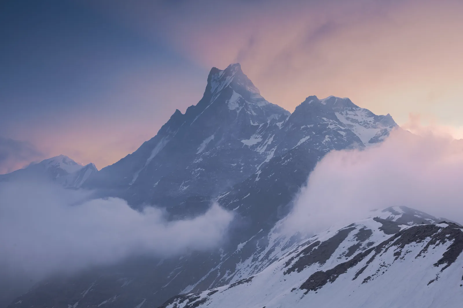 Stunning view of a snow-capped Himalayan mountain peak surrounded by clouds at sunset.
