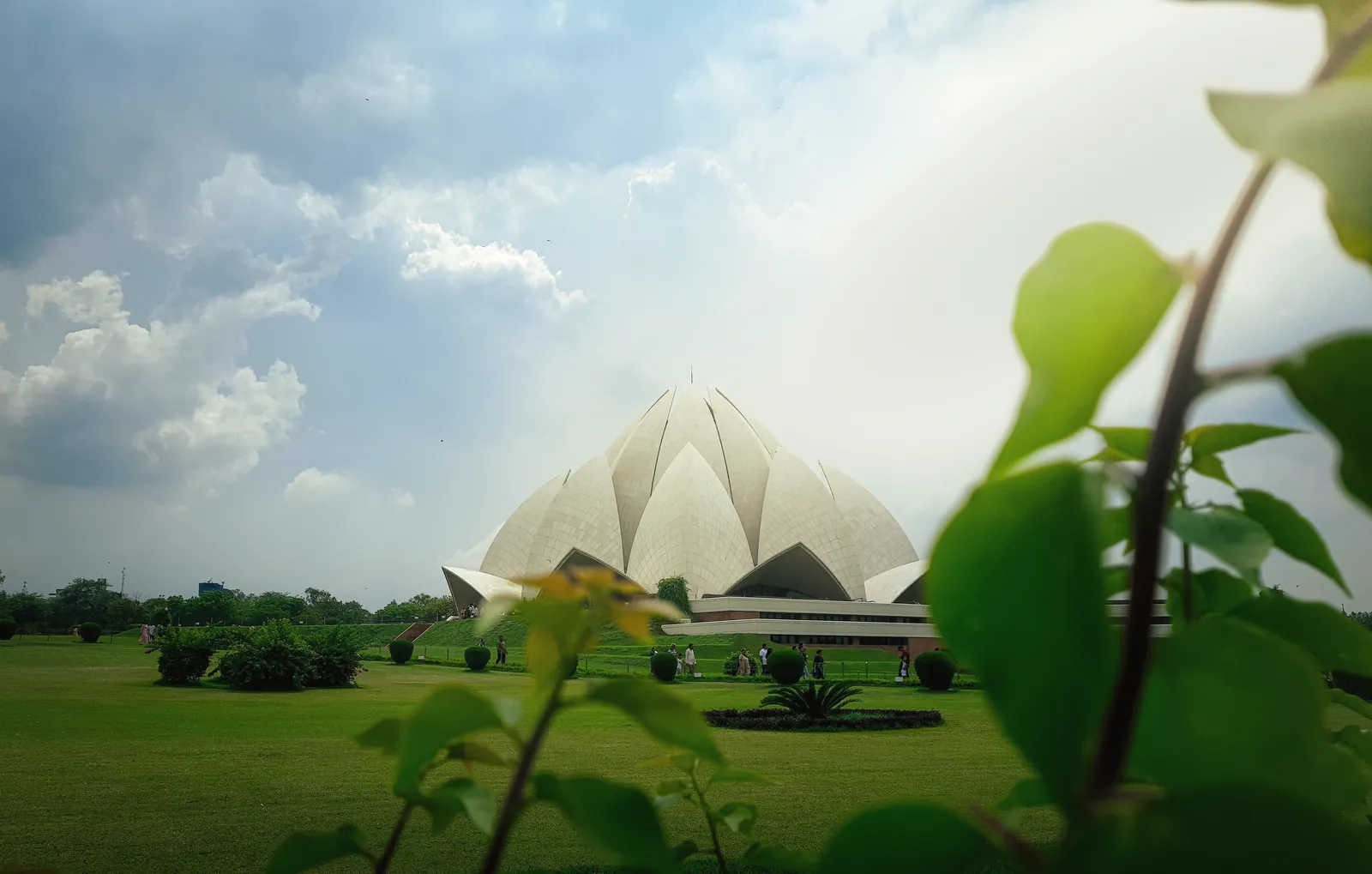 View of the iconic Lotus Temple in New Delhi framed by lush greenery under a cloudy sky.