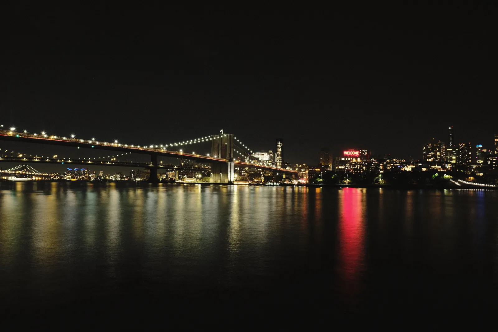 Stunning night view of the illuminated Brooklyn Bridge and NYC skyline reflected on the river.
