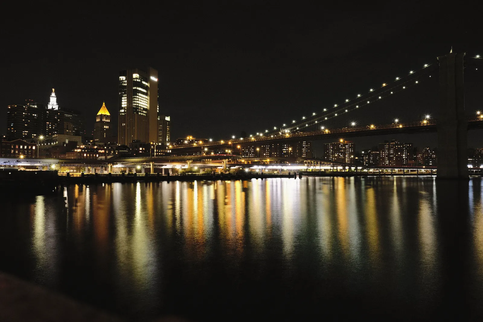 Captivating night view of Brooklyn Bridge and NYC skyline with reflections on water.