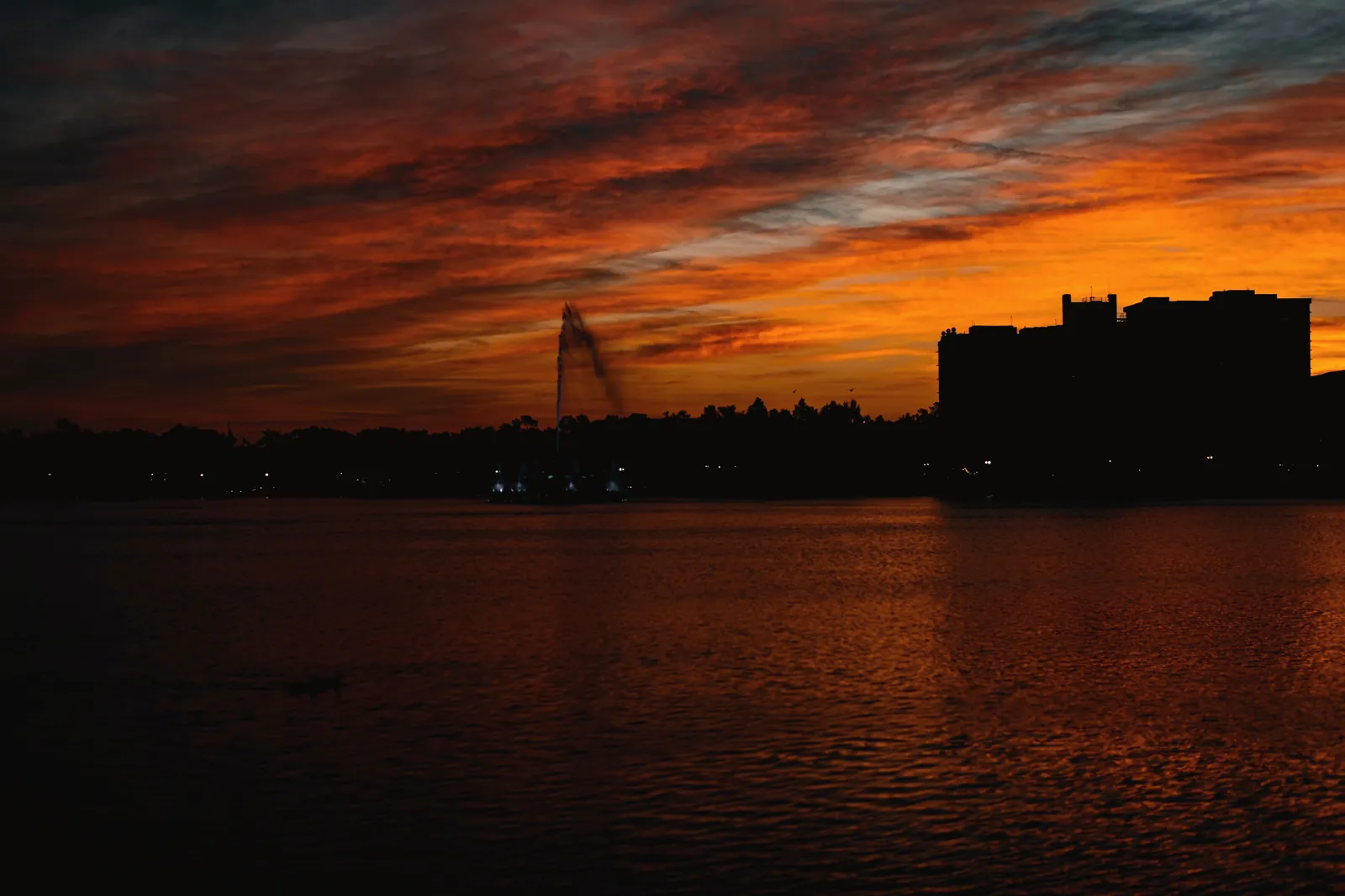 Silhouette of buildings against a vibrant twilight sky over a calm body of water.