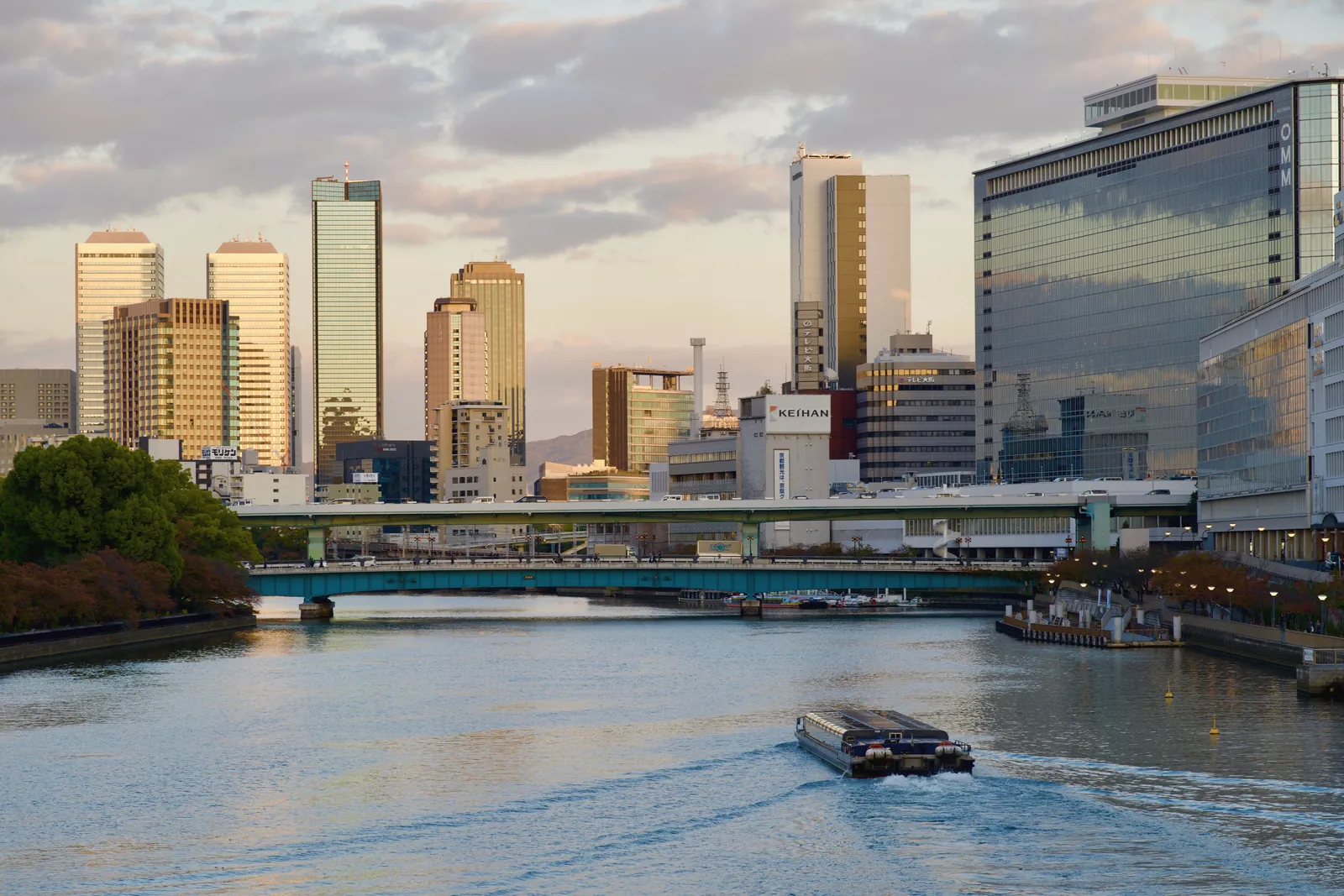 Scenic view of Osaka skyline and river during a calm day. Reflective high-rises and tranquil water create a serene atmosphere.