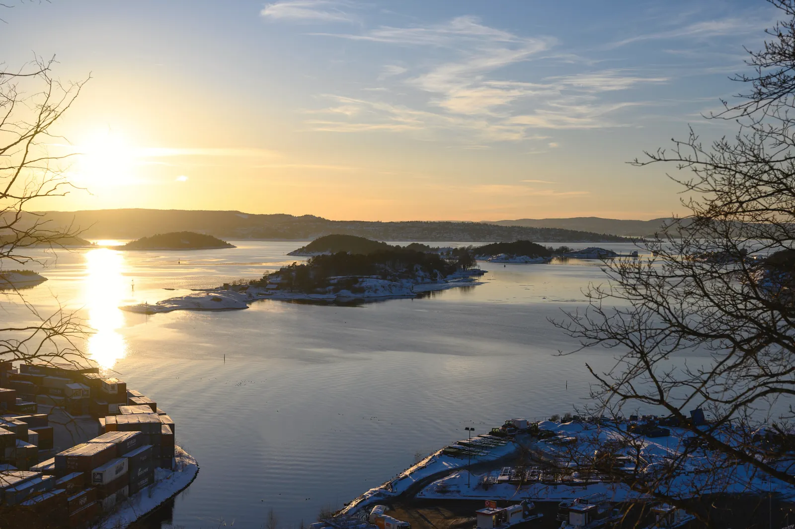 A beautiful winter sunset over Oslo Fjord, highlighting islands and a calm sea with silhouetted trees.