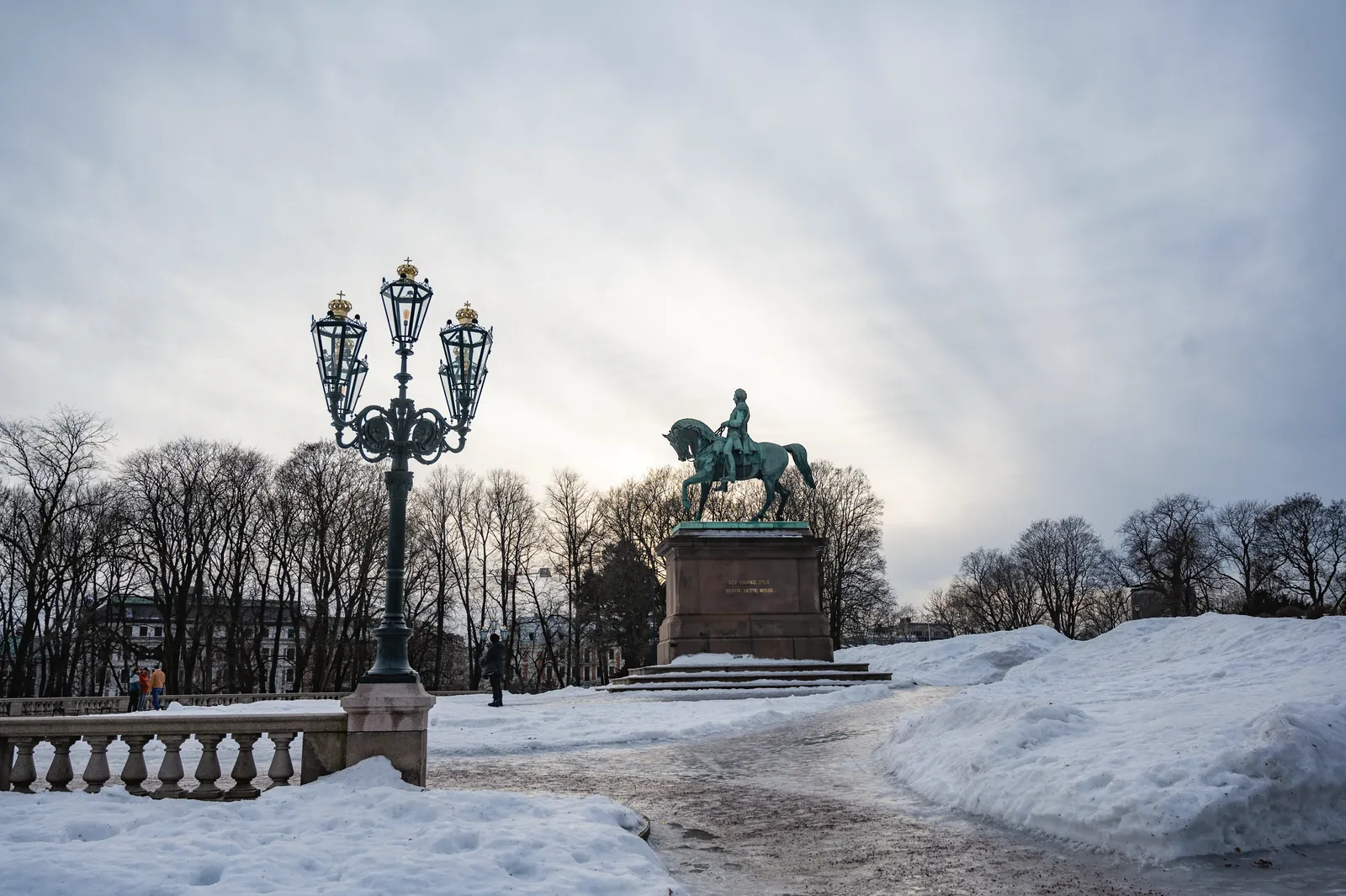 A serene winter scene in an Oslo park featuring a historic equestrian statue surrounded by snow.