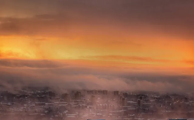 Dramatic aerial view of Oslo skyline enveloped in fog at golden sunset.