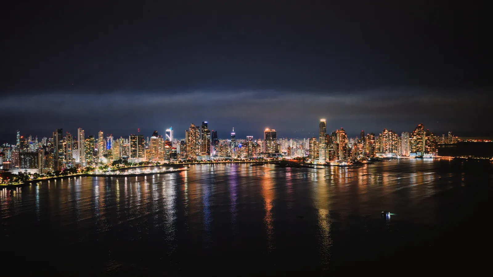 Nighttime aerial view of Panama City's illuminated skyline reflecting on the water.