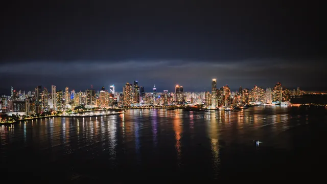 Nighttime aerial view of Panama City's illuminated skyline reflecting on the water.