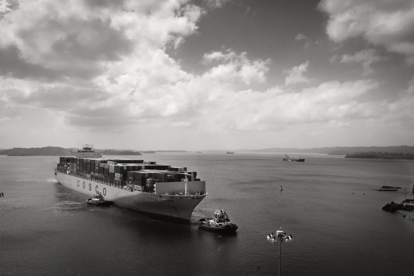 Black and white modern cargo vessel floating on rippling river near small motorboats towards harbor