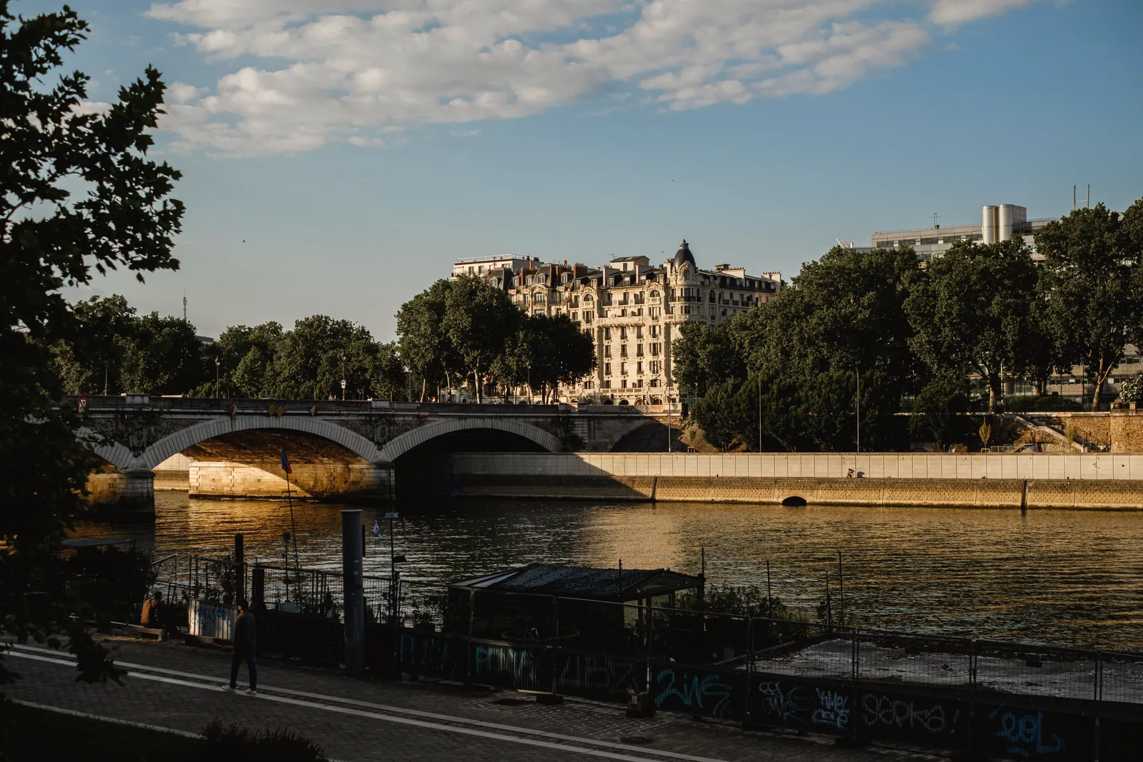 A scenic view of a Parisian bridge and riverbank under warm evening light.