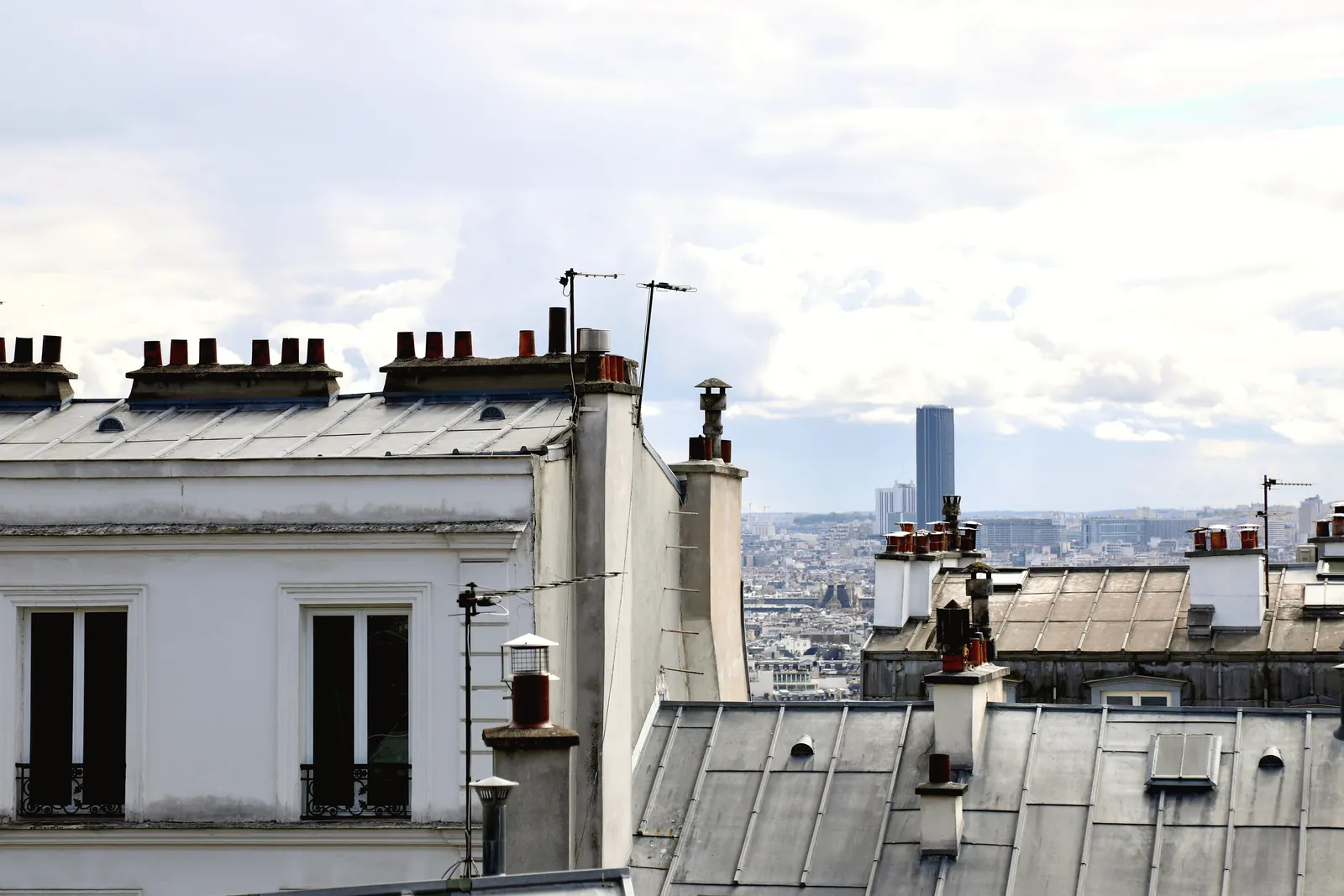 A view of traditional Parisian rooftops with a cityscape in the background under a bright sky.