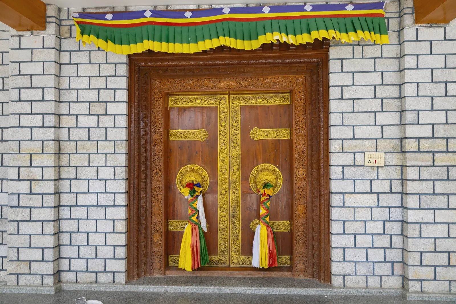 Ornate wooden door with traditional decorations at a temple, featuring colorful tassels and carved patterns.