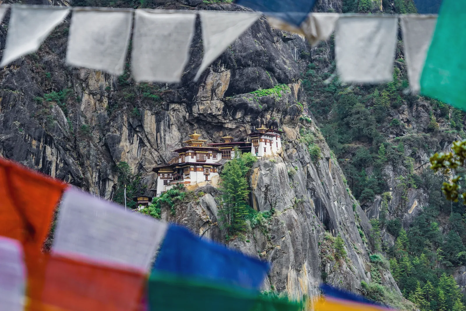 A stunning view of Paro Taktsang Monastery nestled in the cliffs of Bhutan with vibrant prayer flags.