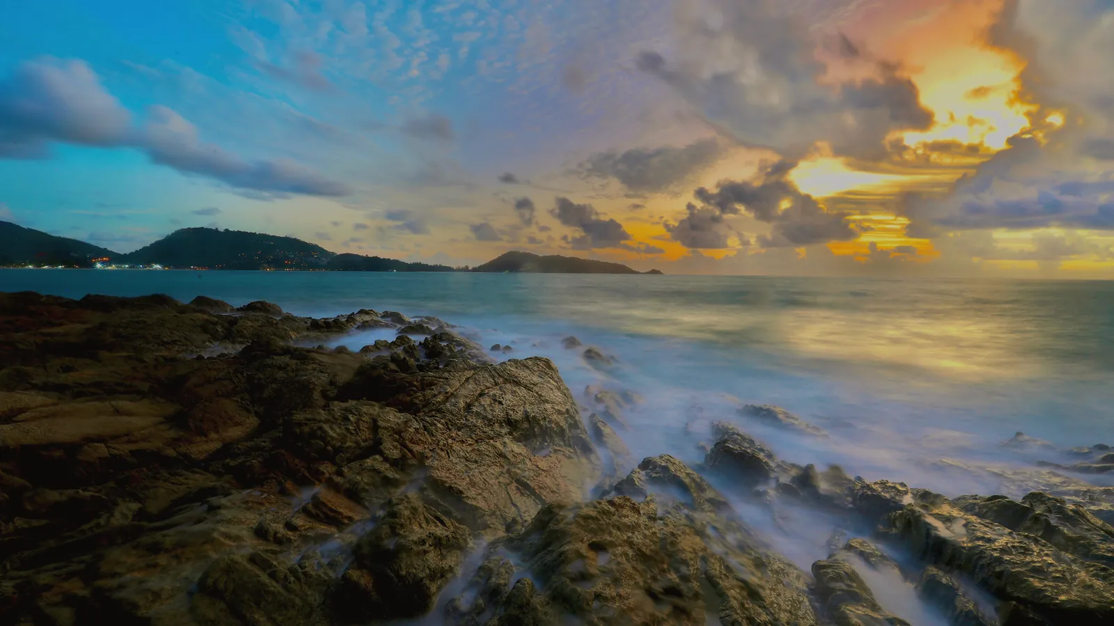Serene view of sunset over rocky coastline at Patong Beach, Phuket, Thailand.