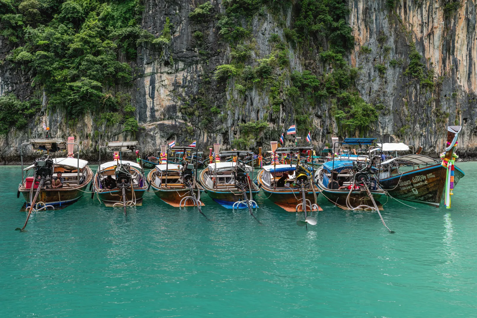 Scenic view of traditional longtail boats moored in Phuket, Thailand with lush cliffs.