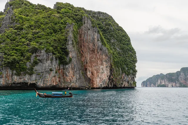 A longtail boat navigating the stunning limestone cliffs of Phuket, Thailand's vibrant ocean landscape.