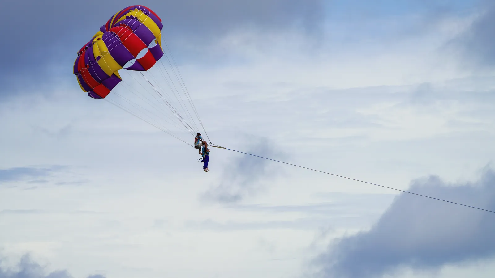 Experience thrilling parasailing over Phuket's stunning beaches with vibrant parachutes against cloudy sky.