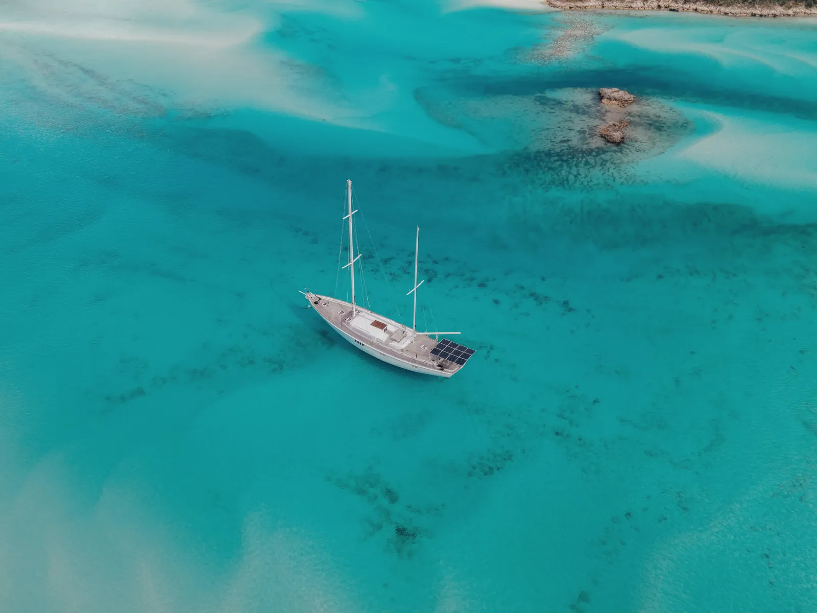 Drone shot of a sailboat on clear turquoise ocean waters.