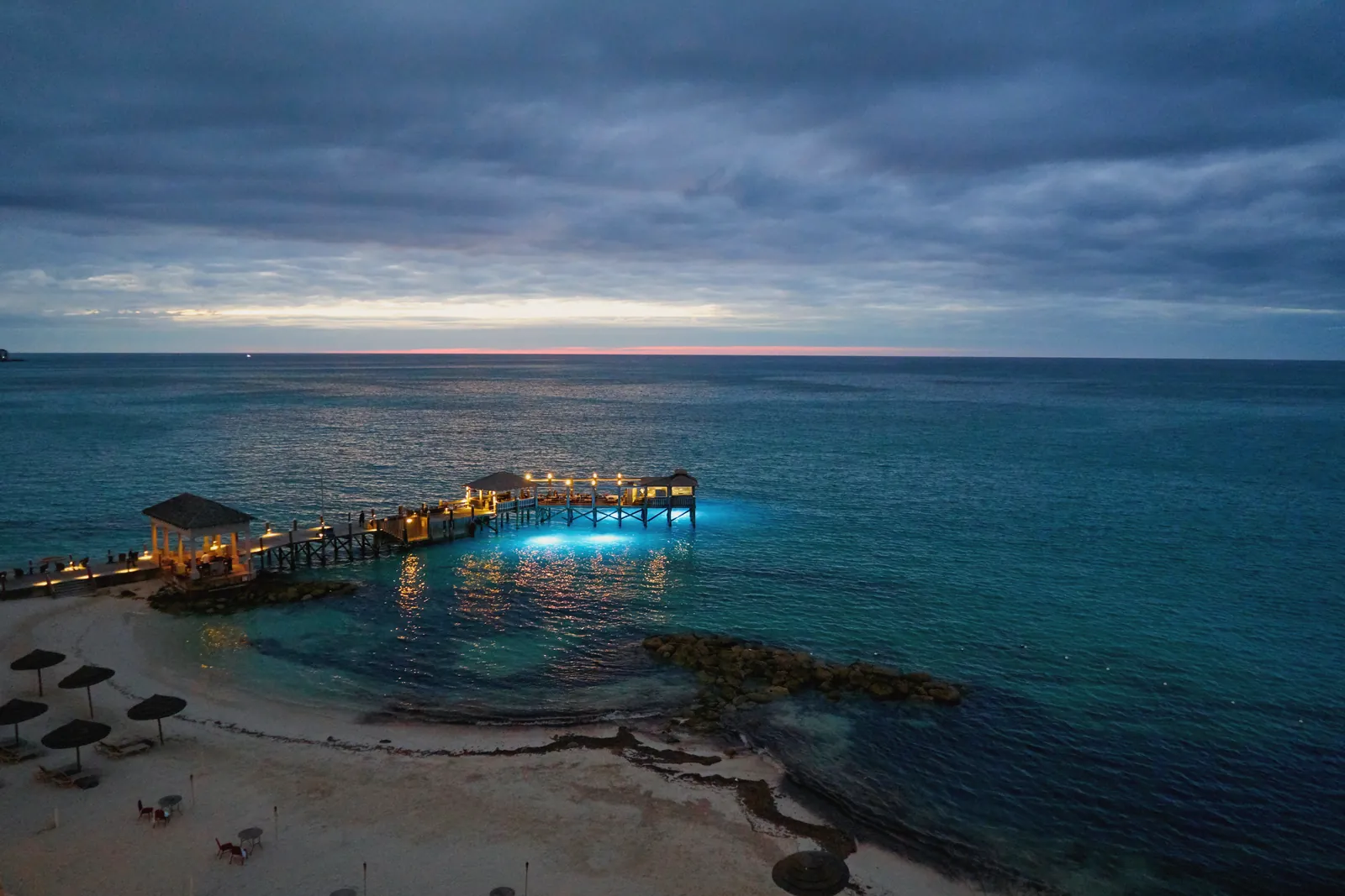 A tranquil seascape at twilight with a pier illuminated over Nassau's blue waters.