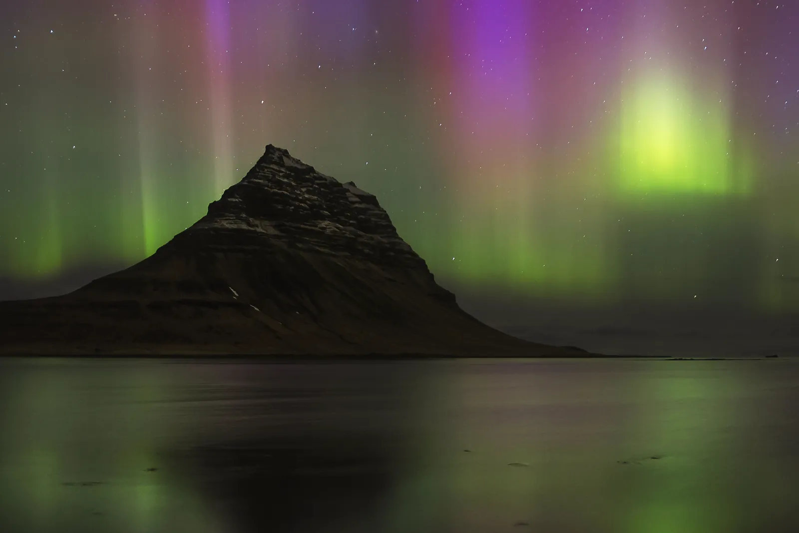 Vibrant northern lights dance over Iceland's iconic Kirkjufell mountain at night.