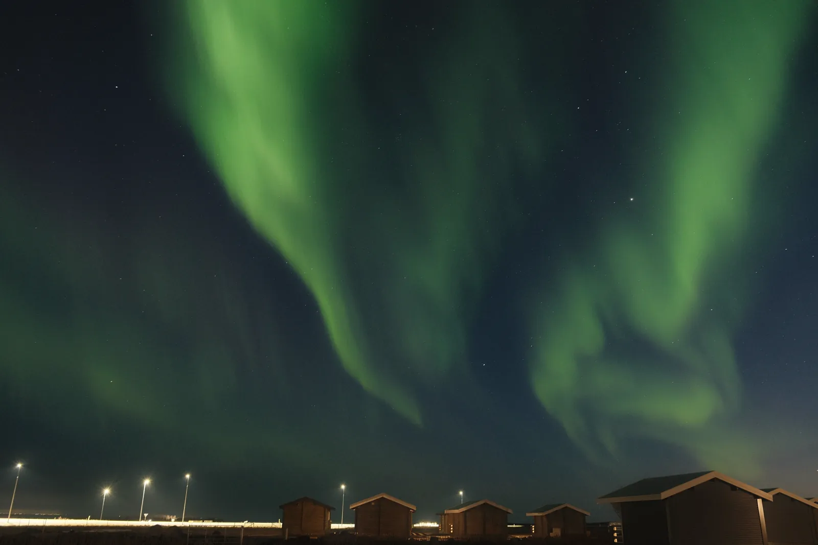 Breathtaking view of the Northern Lights dancing over Icelandic cabins under a starry night sky.