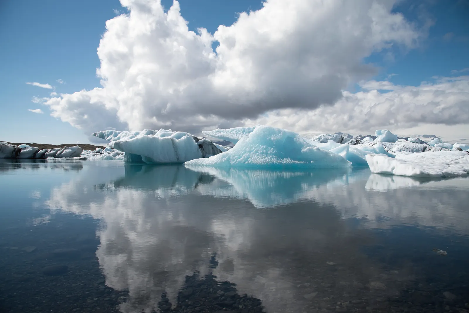 Breathtaking view of icebergs reflecting on a calm glacial lagoon in Iceland under a partly cloudy sky.