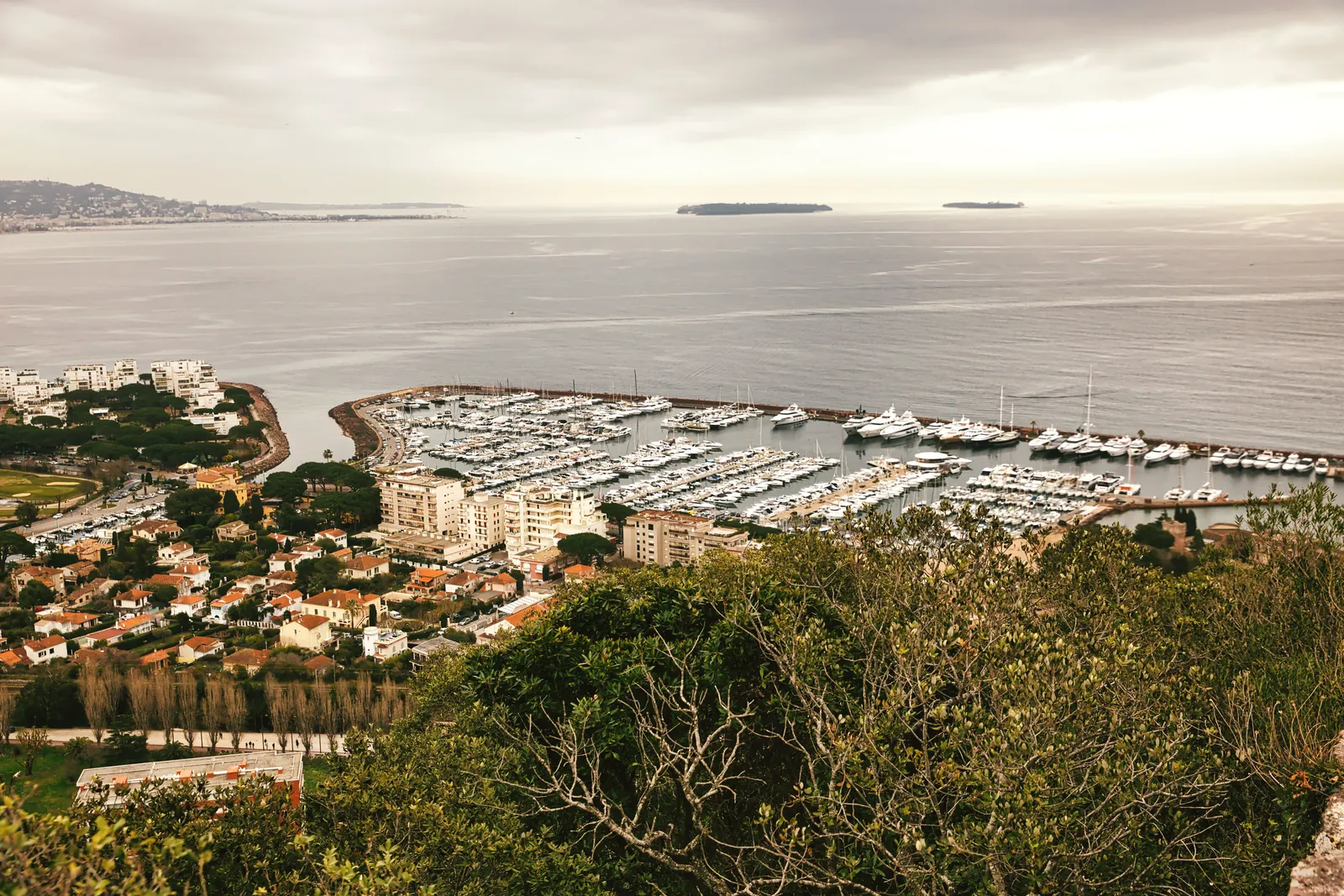 Stunning aerial view of the Cannes Marina and coastal landscape on a cloudy day, highlighting the serene bay area.