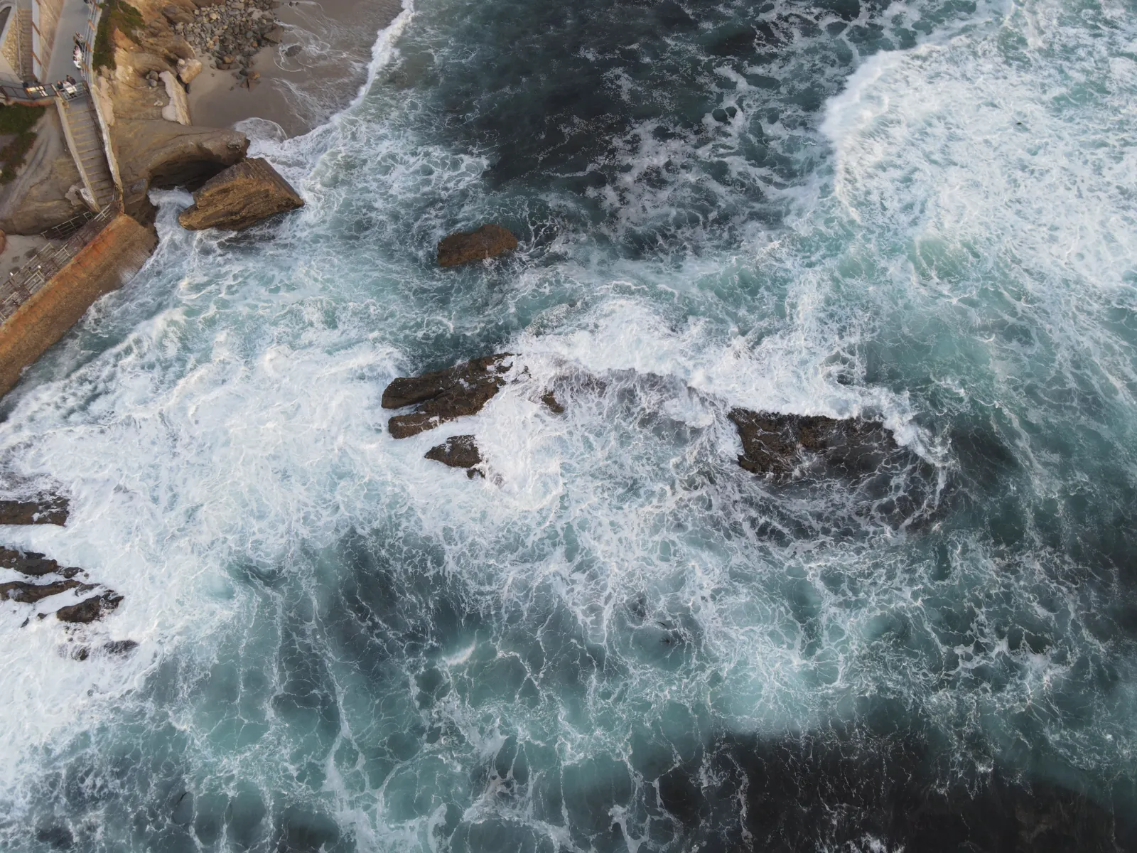 Dynamic aerial shot of waves crashing on rocky California coastline, showcasing nature's power.