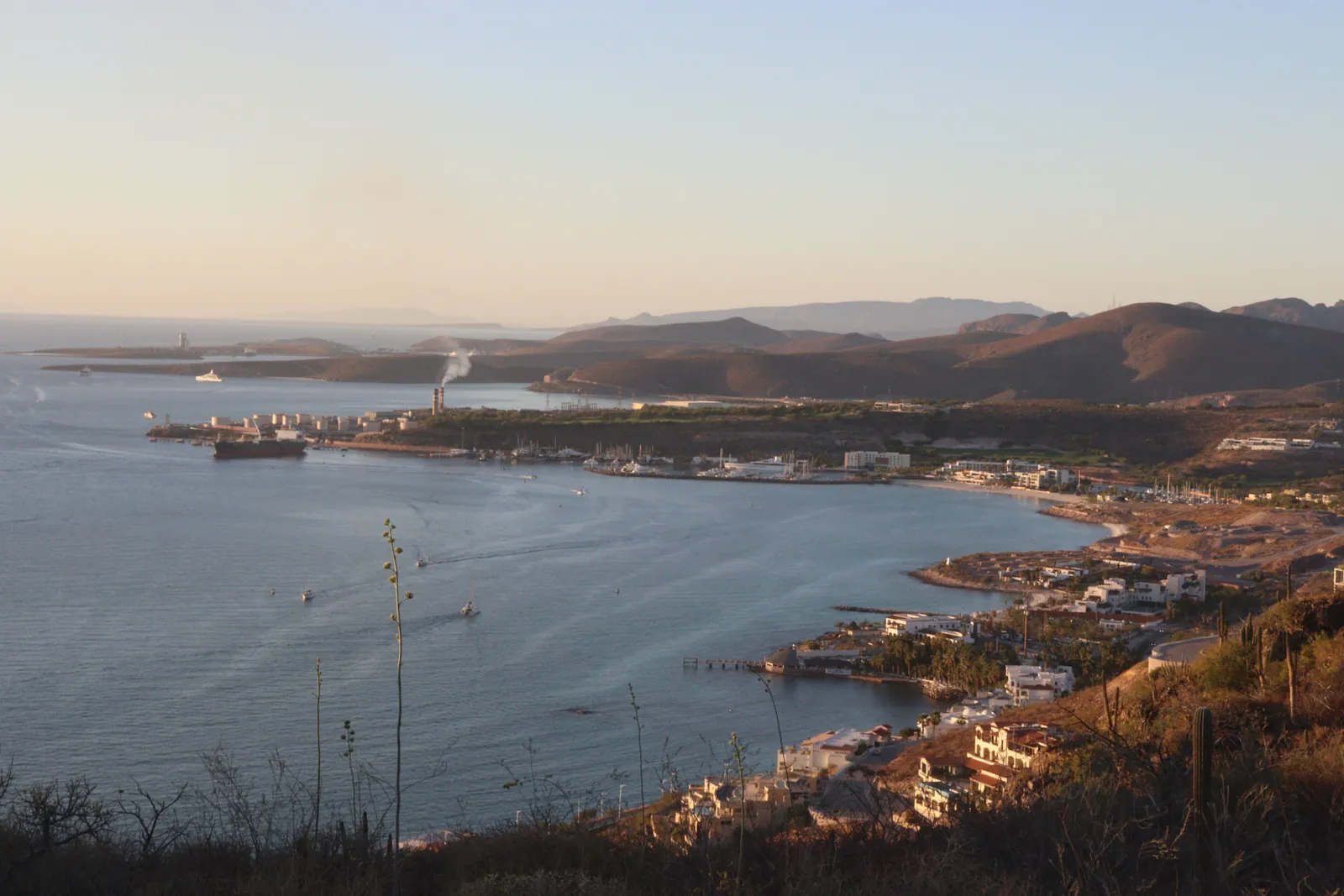 Scenic aerial view of a coastal port city with mountains, at sunrise, capturing serene waters and surrounding landscape.