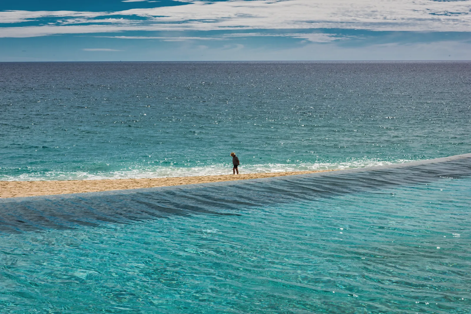 A lone person strolls along the serene beach in San José del Cabo, Mexico under a bright blue sky.
