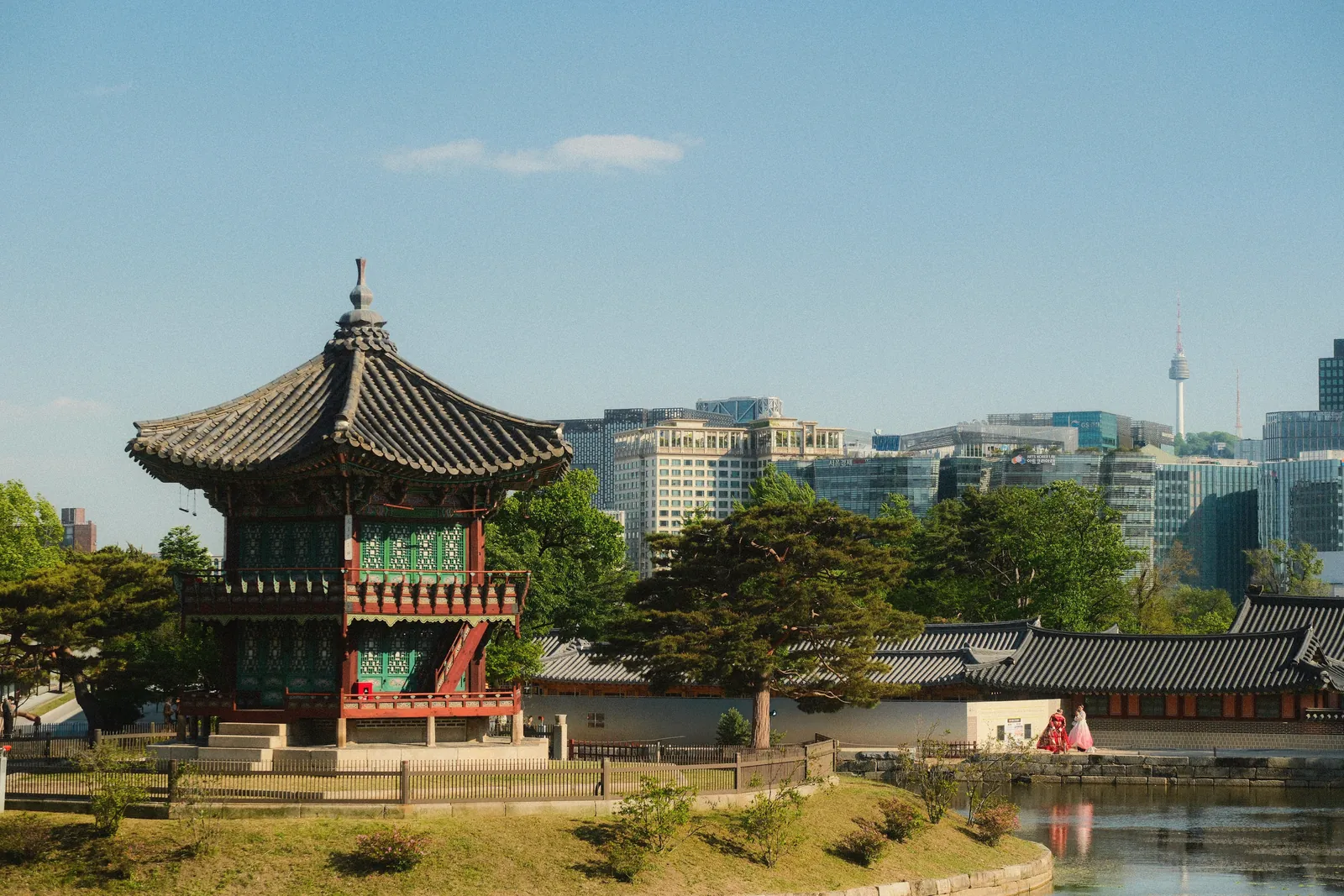 A traditional Korean pagoda in a serene park with a modern city skyline in the background, showcasing cultural contrast.
