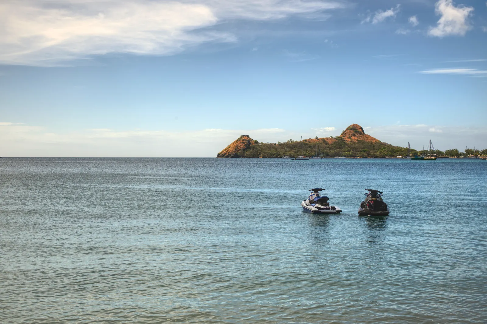 Idyllic tropical beachscape with two jet skis on calm ocean waters at sunset.