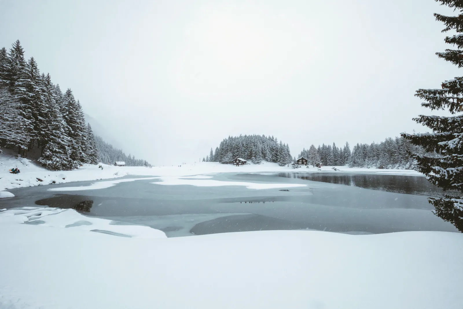 A tranquil winter scene of a snow-covered lake surrounded by forests and cabins.